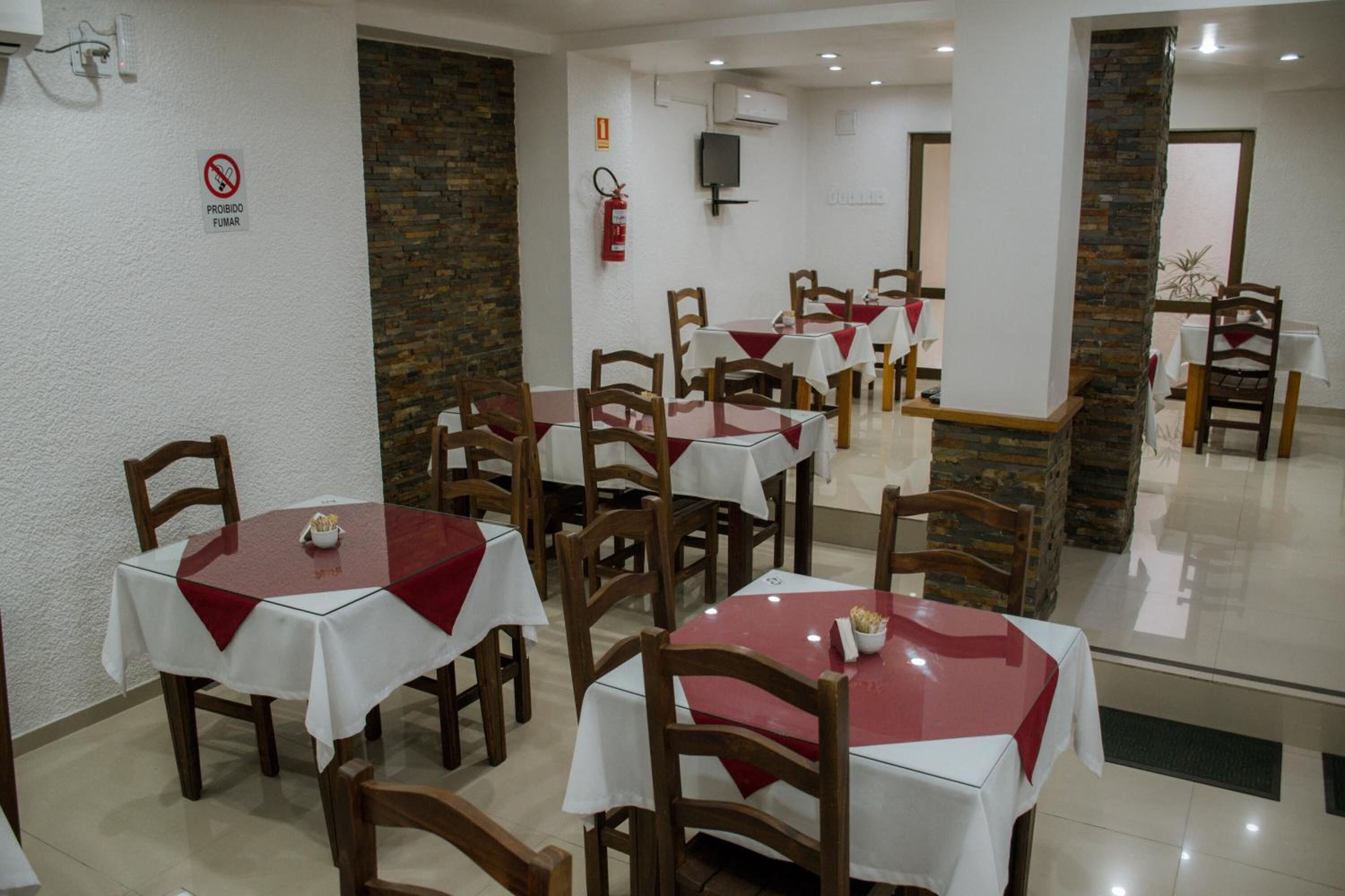 A restaurant with round tables covered with white and red tablecloths, wooden chairs, and stone pillars.