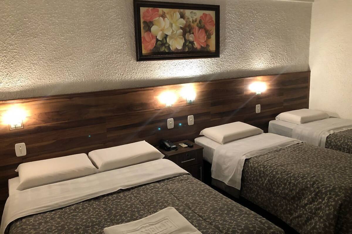 A hotel room with four beds, a wooden headboard, a painting of flowers, and a nightstand with a phone and lamp.