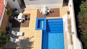Una piscina en la azotea con solárium, sillones de descanso y una mesa pequeña.