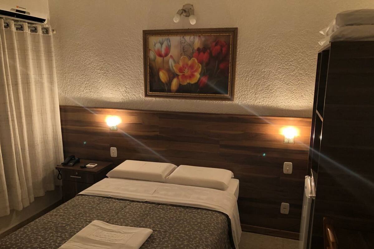 A hotel room with a bed, a nightstand, a telephone, and a painting on the wall.