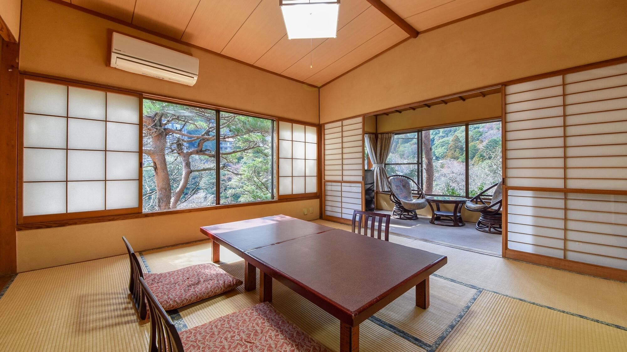A traditional Japanese room with tatami flooring, a wooden table, and a view of a forest through large shoji screens.