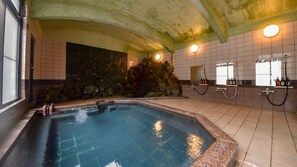 A swimming pool with a stone wall and a large rock formation, a shower area with bottles, and a window with a view. - Yunoyama Onsen Sankei-en (Komono)