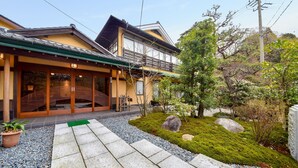 Una casa japonesa tradicional con fachada de madera, puertas correderas y un pequeño jardín de rocas y musgo.