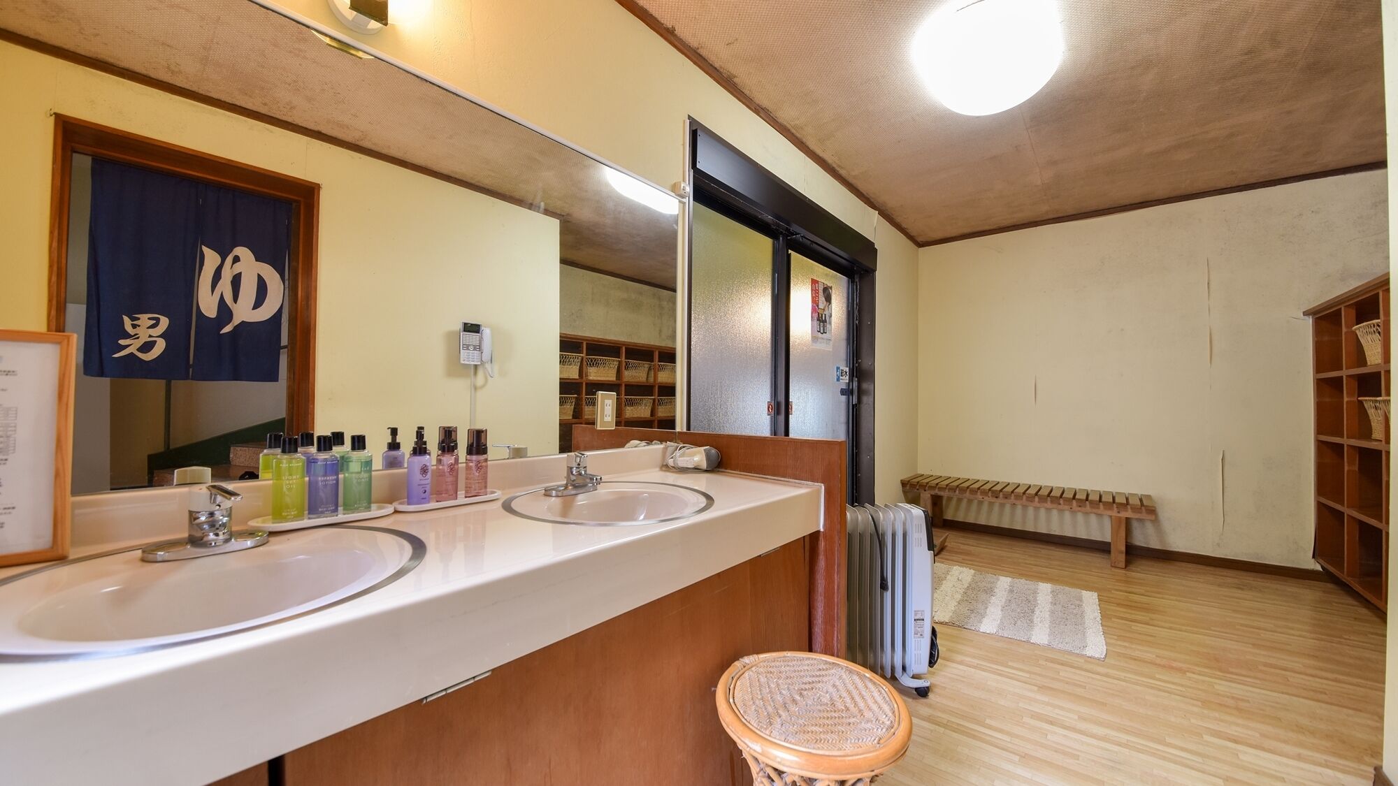 Un baño de hotel con dos lavamanos, un espejo grande, un teléfono y un banco de madera.