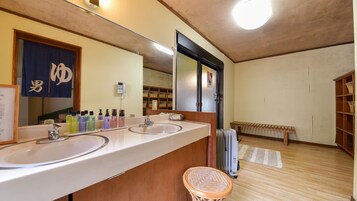 Un baño de hotel con dos lavamanos, un espejo grande, un teléfono y un banco de madera.