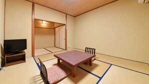 Una habitación japonesa tradicional con suelo de tatami, una mesa baja, dos sillas y un televisor sobre un soporte de madera.