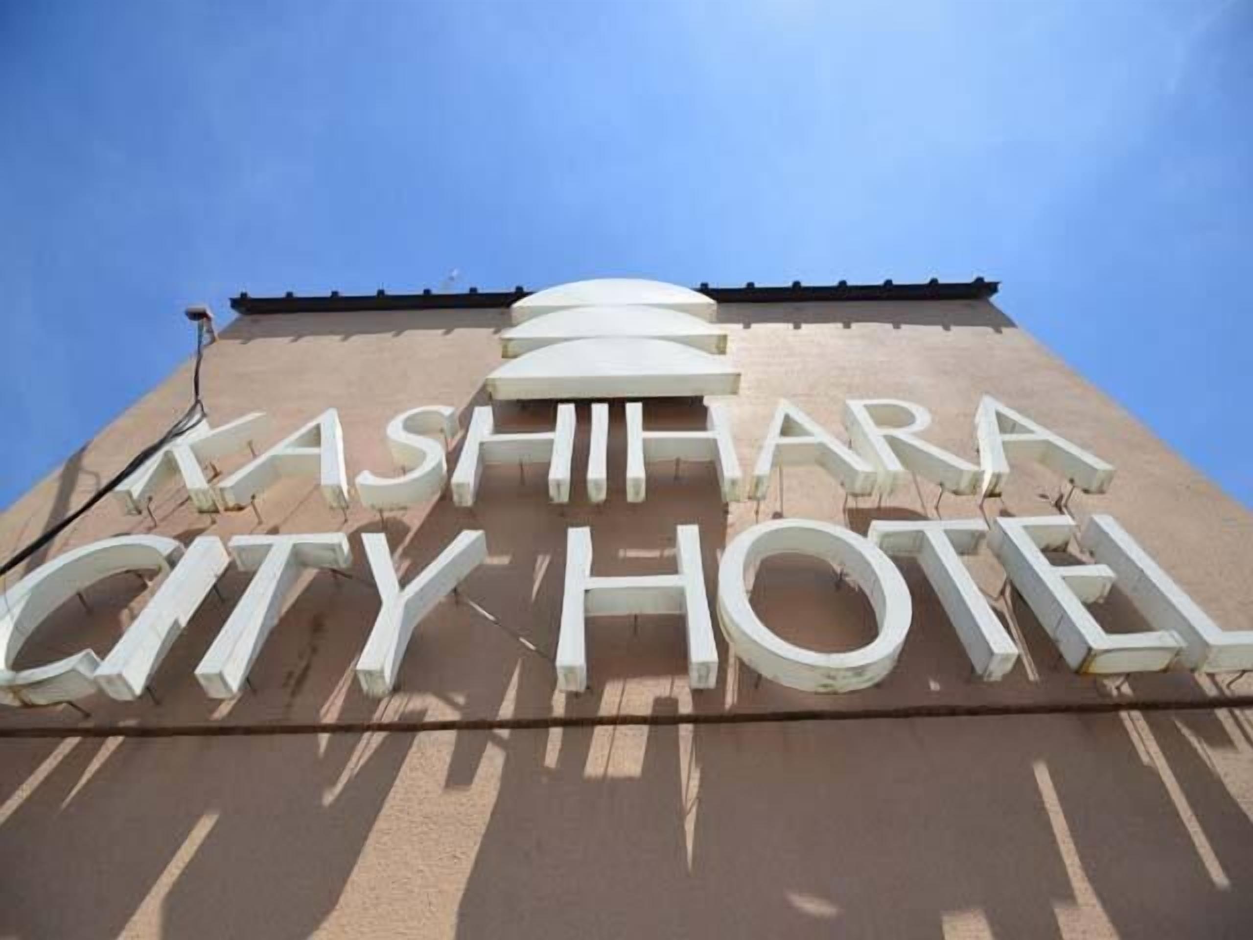 A large, white sign for the Ashihara City Hotel with a clear blue sky in the background.