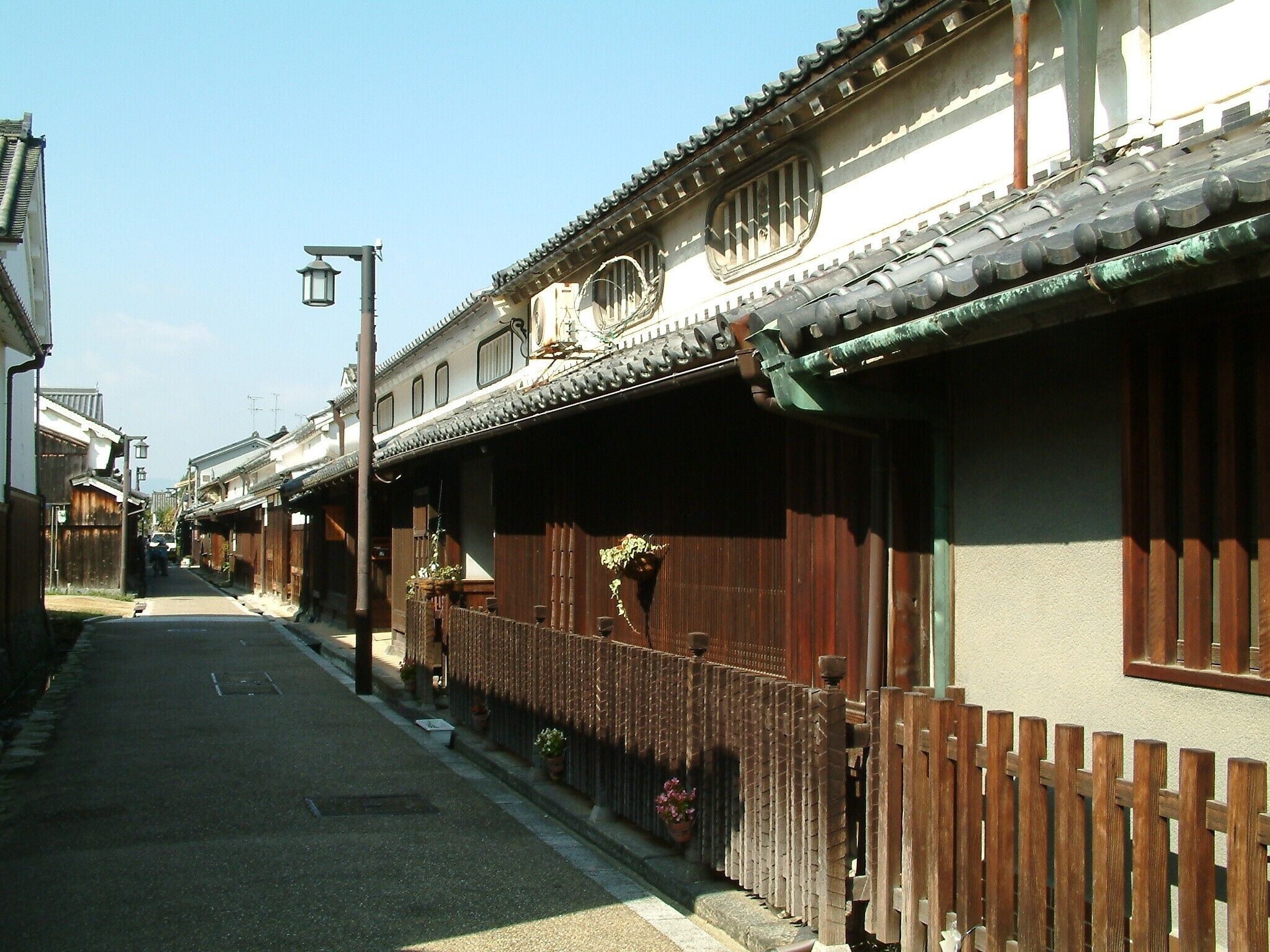 A narrow street lined with traditional wooden houses, each with a tiled roof and wooden fences.