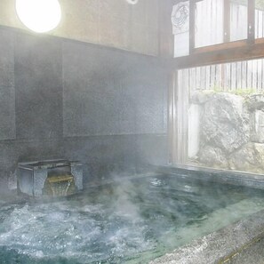 Un baño de aguas termales con una pared de piedra y una valla de madera al fondo.