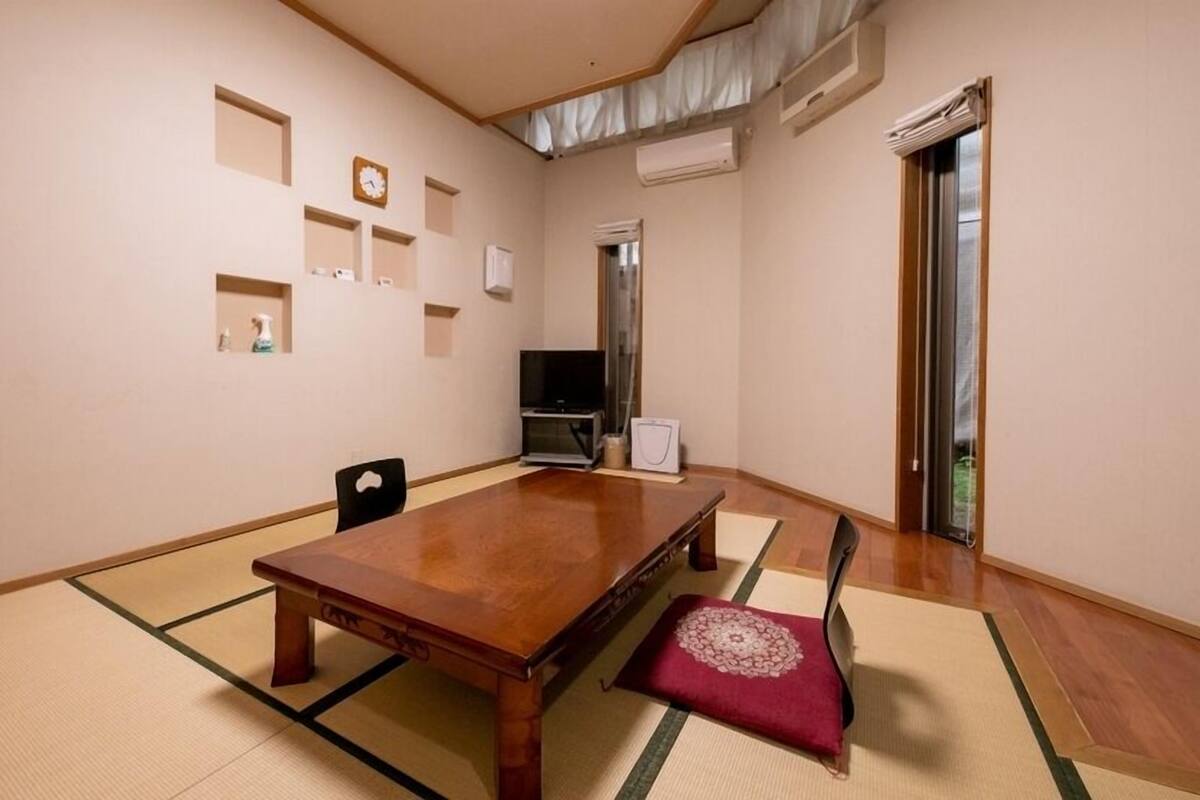 Una stanza tradizionale con tatami, un tavolo in legno, sedute su tatami, una televisione e una porta scorrevole.