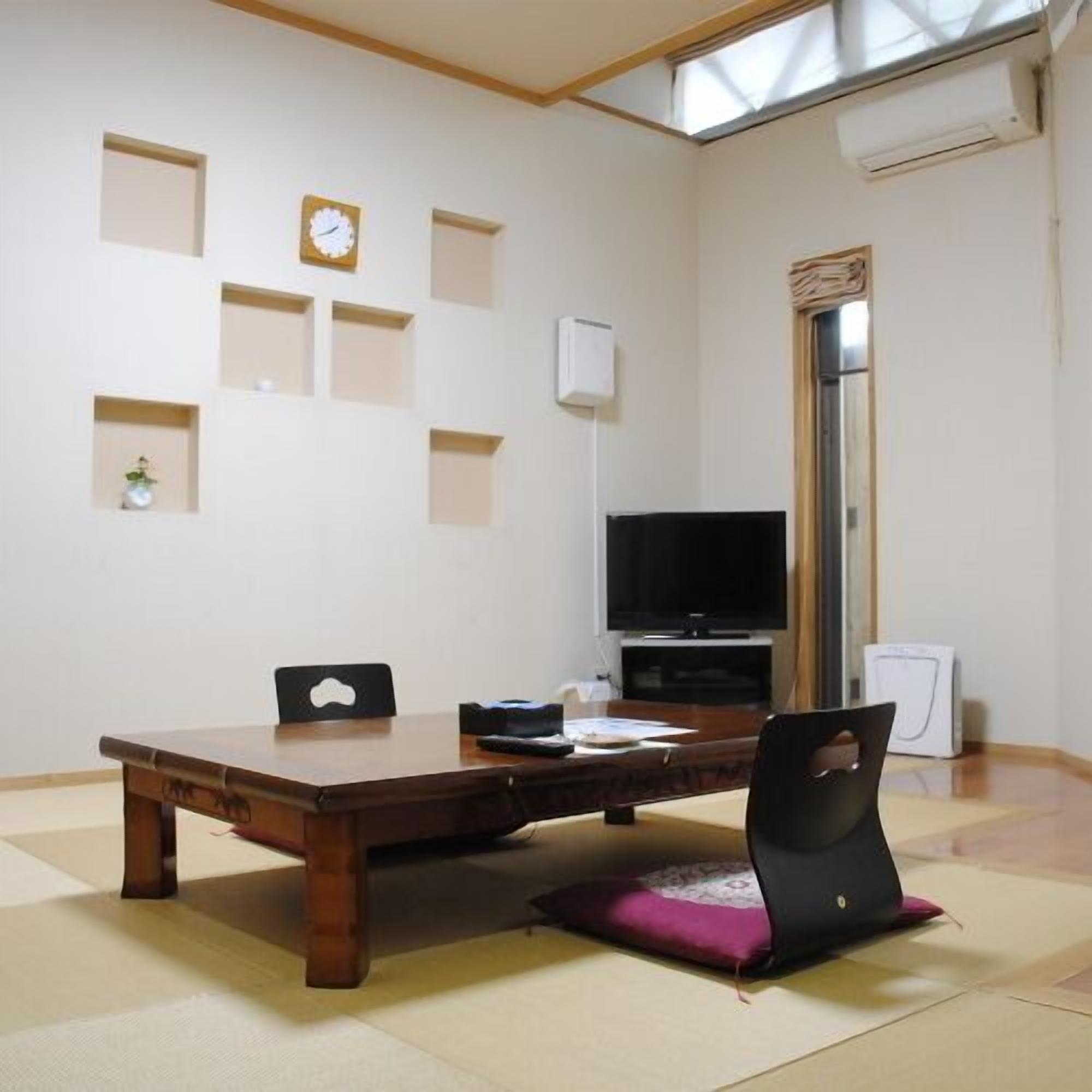 Een kamer met een houten tafel, stoelen, een televisie en een klok aan de muur.