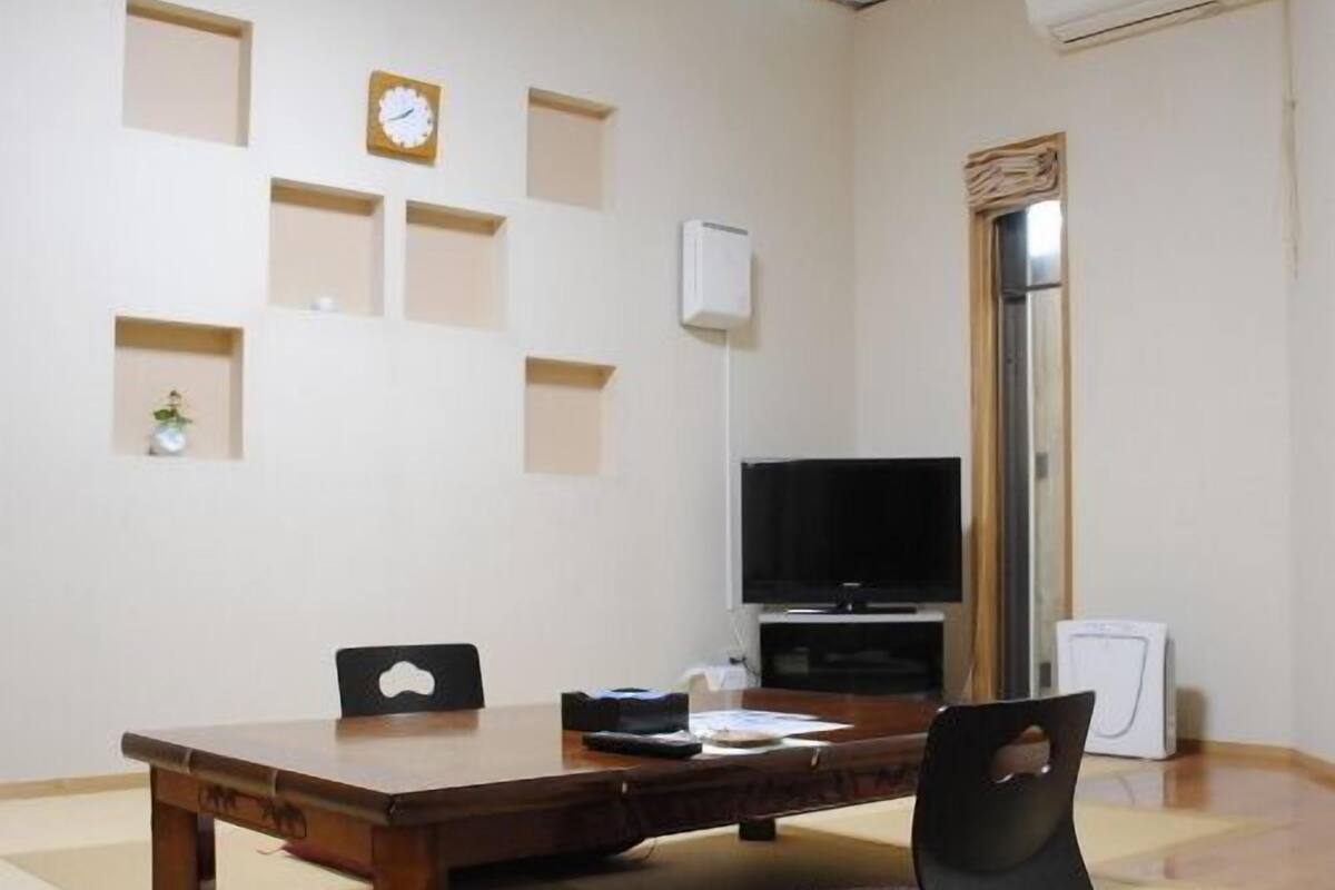 Una stanza con un tavolo di legno, sedie, una televisione e un orologio appeso al muro.