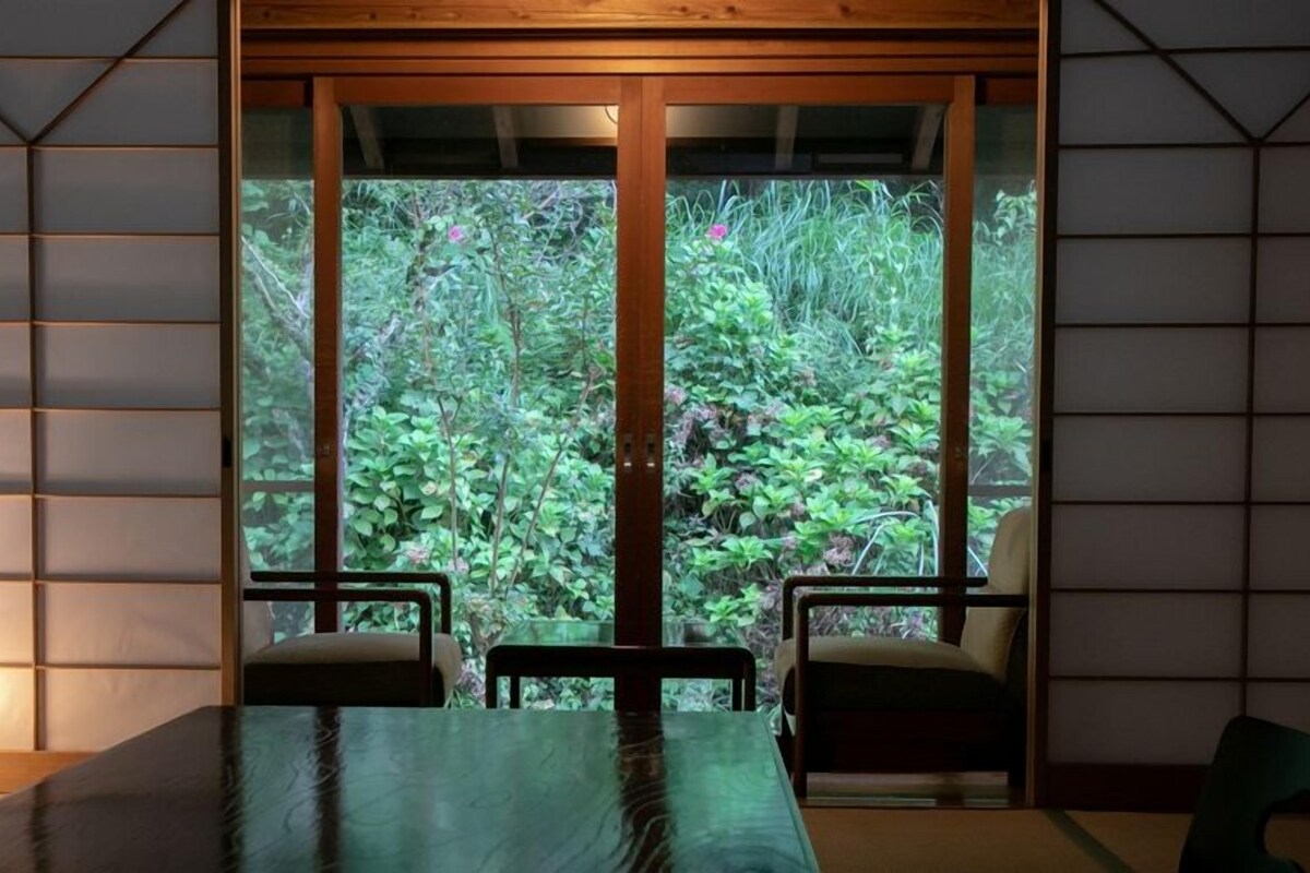 A room with a large window, a table, two chairs, and a lamp.