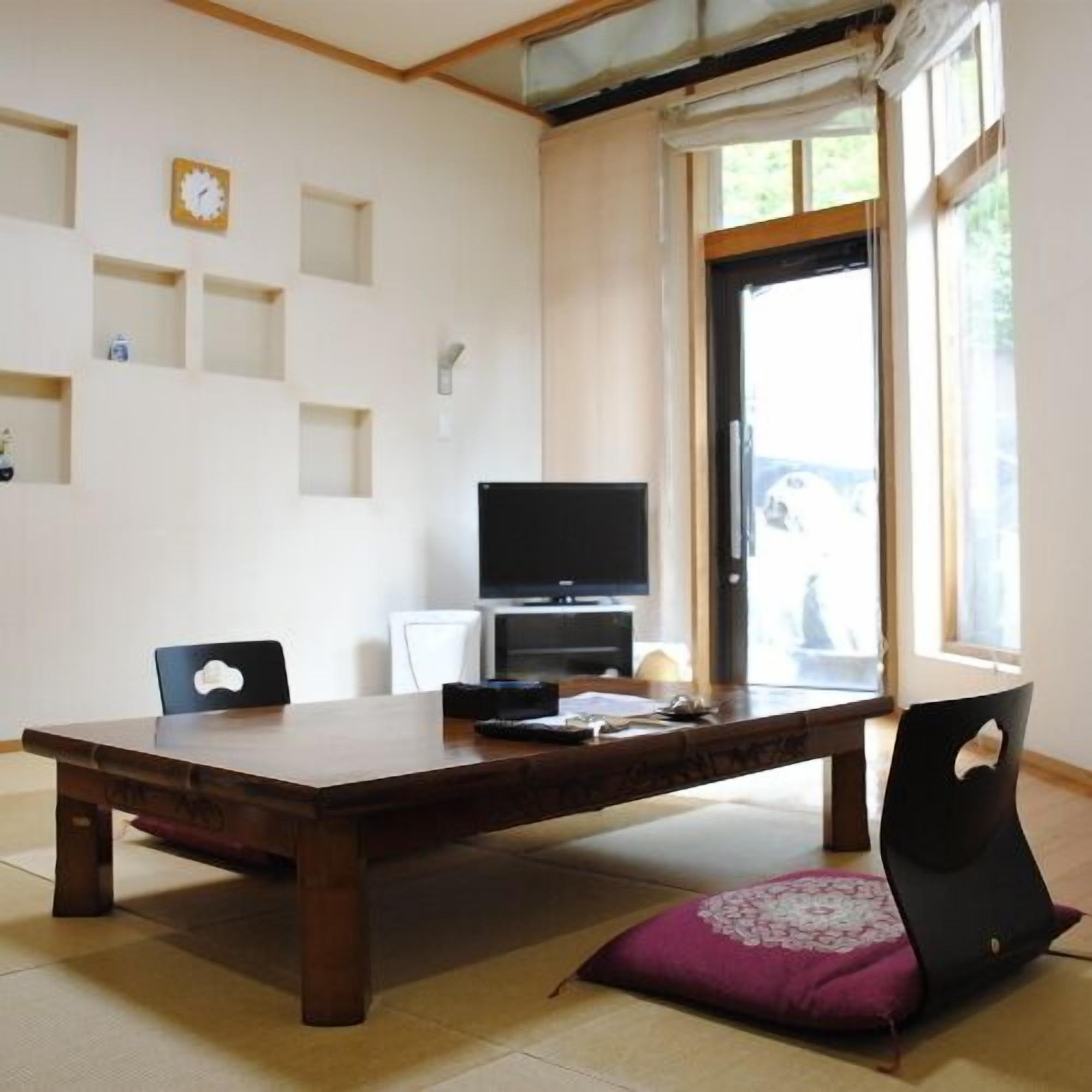 Een kamer met een houten eettafel, stoelen, een televisie en een raam met uitzicht.