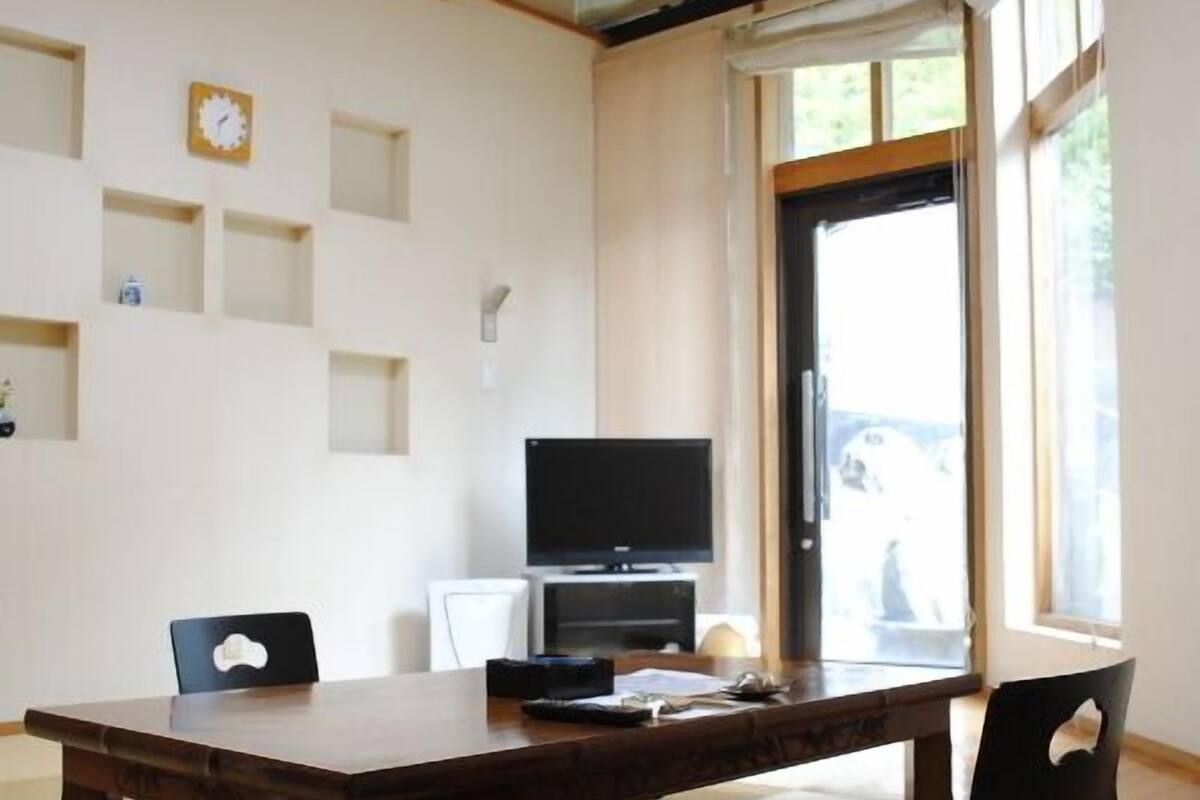 Una stanza con un tavolo da pranzo in legno, sedie, una televisione e una finestra vista.