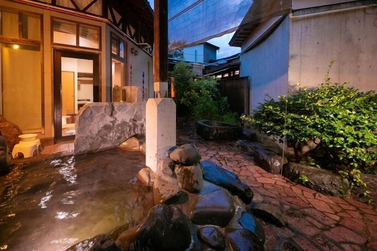 Un giardino tradizionale giapponese con uno stagno in pietra, strutture in legno e vegetazione lussureggiante.