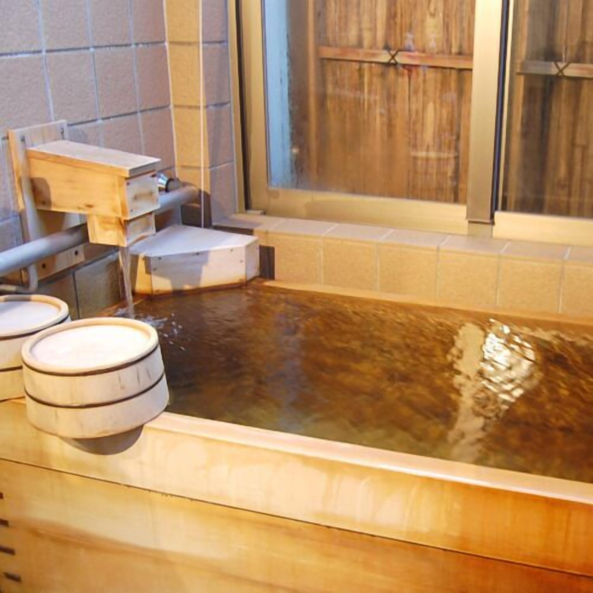 A hot spring bath with wooden stools, a wooden bench, and a tiled wall.