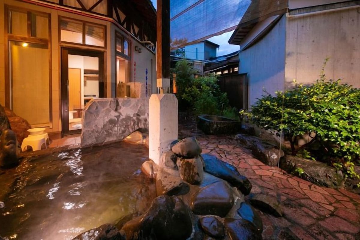 A traditional Japanese garden with a stone pond, wooden structures, and lush greenery.