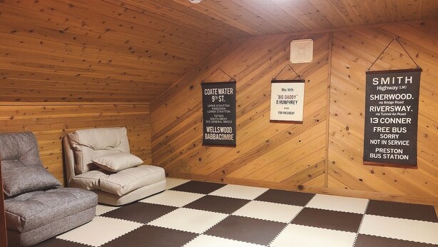 Un cuarto ático acogedor con piso a cuadros, un sillón gris y dos carteles en las paredes.