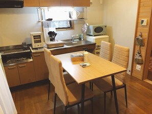 A compact kitchen with a microwave, toaster, and a small refrigerator. There is a dining table with chairs and a window above the sink. - Kyoto Maizuru Fururu Farm Cottage (Maizuru)