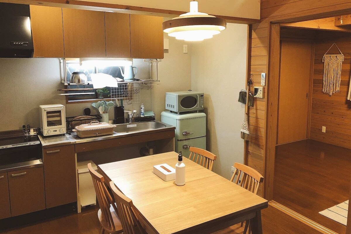 Una cocina compacta con armarios de madera, un microondas, un tostador y un adorno de macramé colgado en la pared.