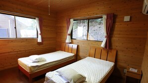 Una cabaña con dos camas de madera, paredes de madera y una ventana con cortinas.