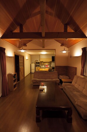 A cozy living room with a wooden ceiling, a sofa, a coffee table, and a kitchen in the background. - Kyoto Maizuru Fururu Farm Cottage (Maizuru)