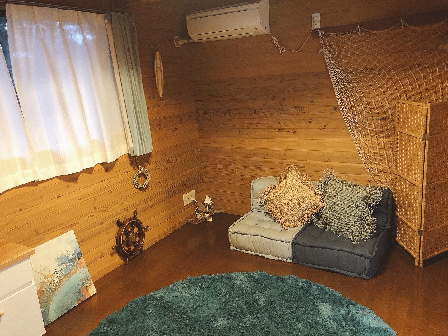 A cozy room with wooden walls, a sofa with cushions, a small rug, and a decorative wheel.