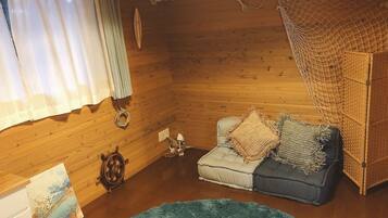 A cozy room with wooden walls, a sofa with cushions, a small rug, and a decorative wheel.
