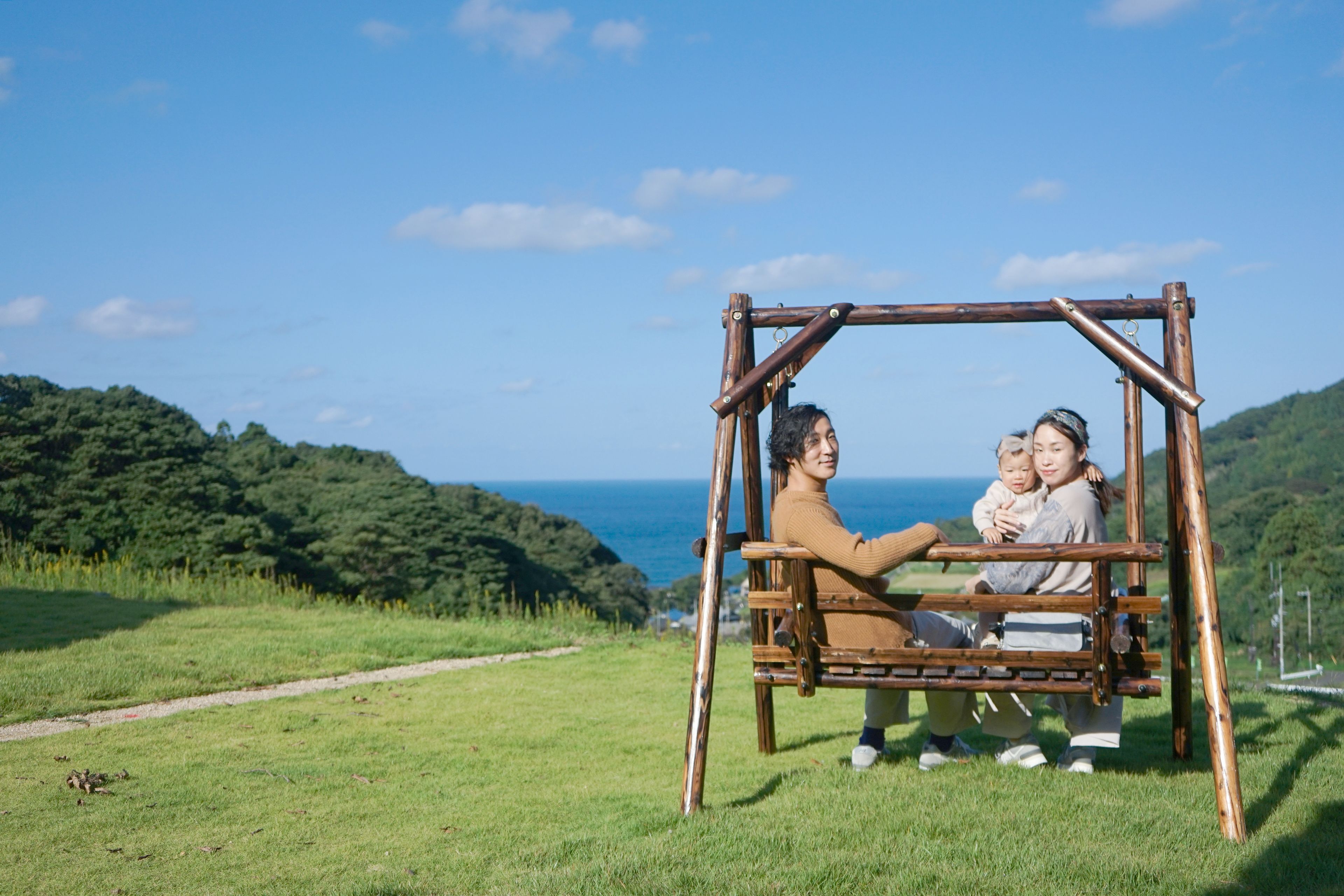 A wooden swing set in a grassy field with a view of the sea and hills.