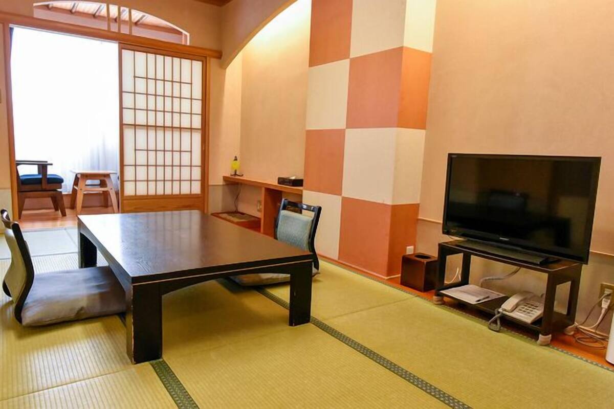Une pièce de style japonais traditionnel, avec un sol recouvert de tatamis, une table basse, un téléviseur et une porte coulissante.