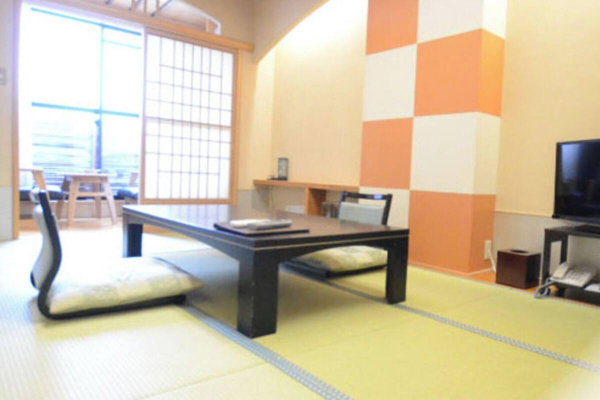 Une pièce traditionnelle avec un sol recouvert de tatamis, une petite table basse, des coussins et un téléviseur.