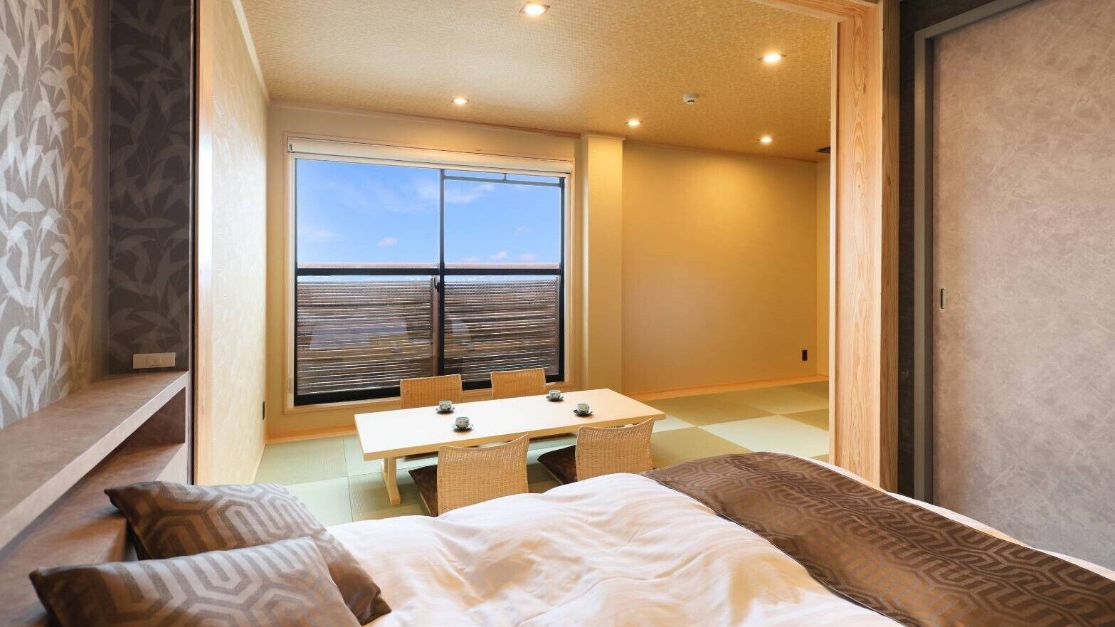 Un hotel moderno con una cama grande, una mesa de comedor y vistas al mar a través de un ventanal amplio.