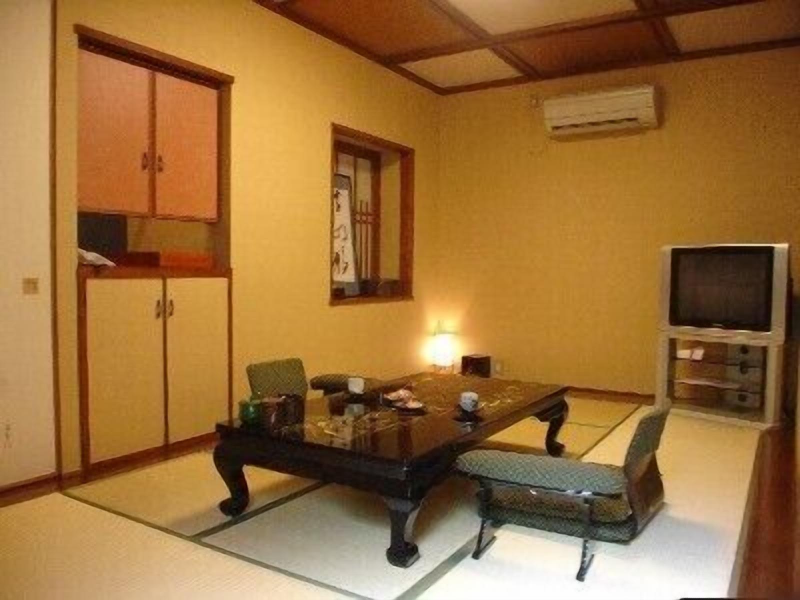 Una habitación de estilo japonés tradicional con suelo de tatami, una mesa baja, sillas, un televisor y un armario.