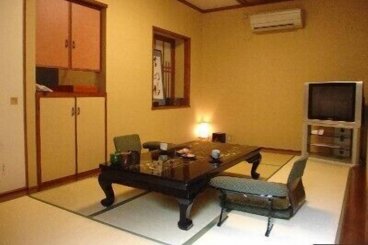 Une pièce de style japonais traditionnel, avec un sol recouvert de tatamis, une table basse, des chaises, un téléviseur et un meuble.