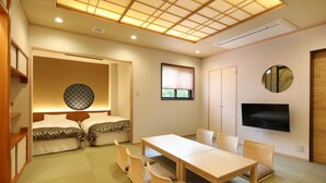 A room with two beds, a dining table, chairs, a TV, and a ceiling with a grid pattern.