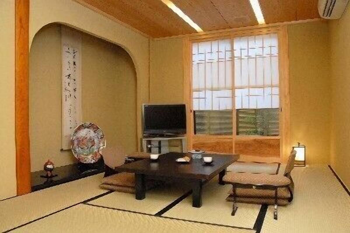 Une pièce de style japonais traditionnel, avec un sol recouvert de tatamis, une table basse, un téléviseur et une porte coulissante.