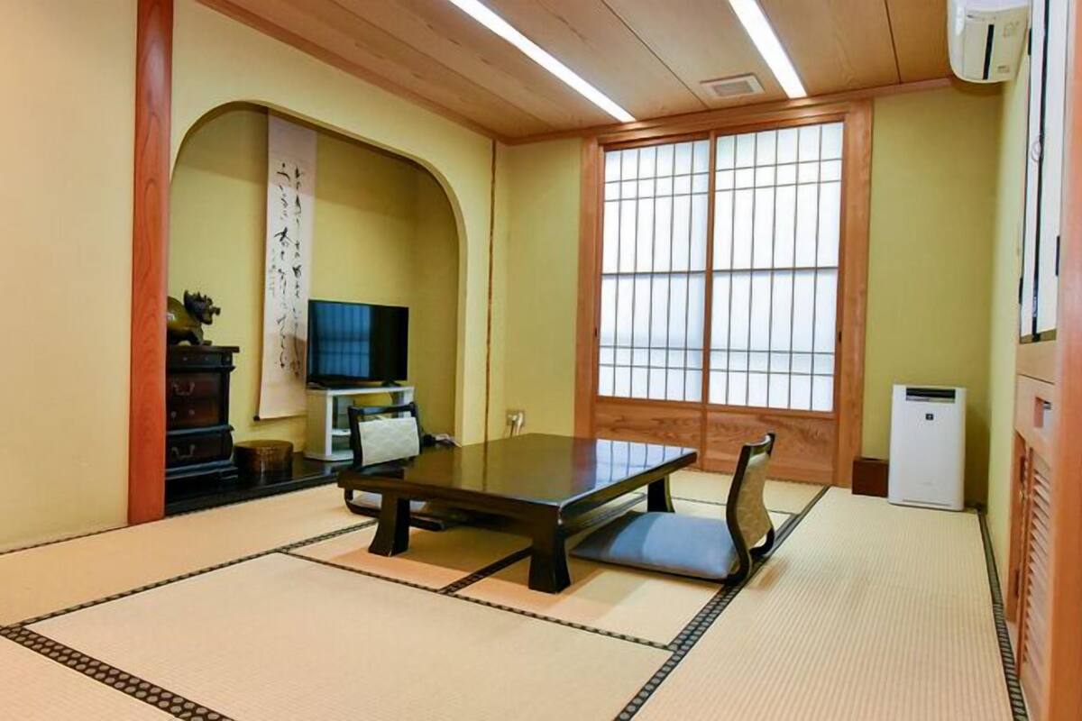 Une pièce de style japonais traditionnel, avec un sol recouvert de tatamis, une table basse, un téléviseur et des portes coulissantes.