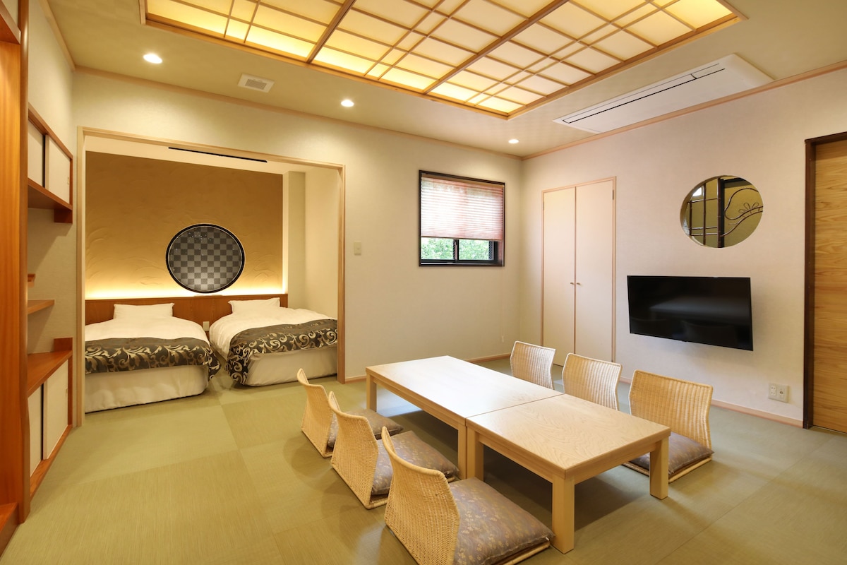 A room with two beds, a dining table, chairs, a TV, and a ceiling with a grid pattern.