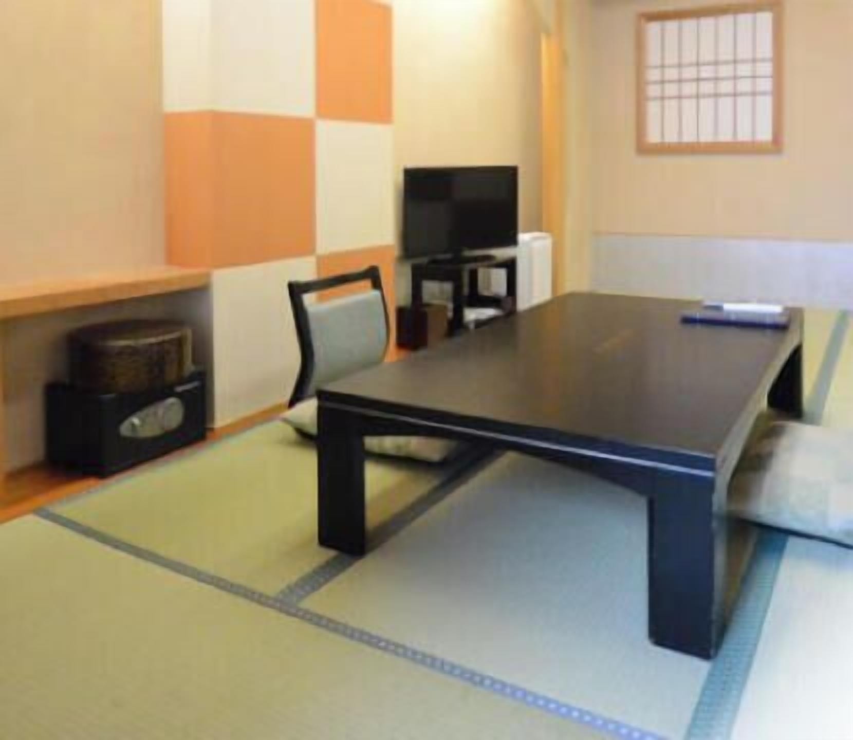 Una habitación con suelo de tatami, una mesa baja, una silla, un televisor y un estante con un altavoz.