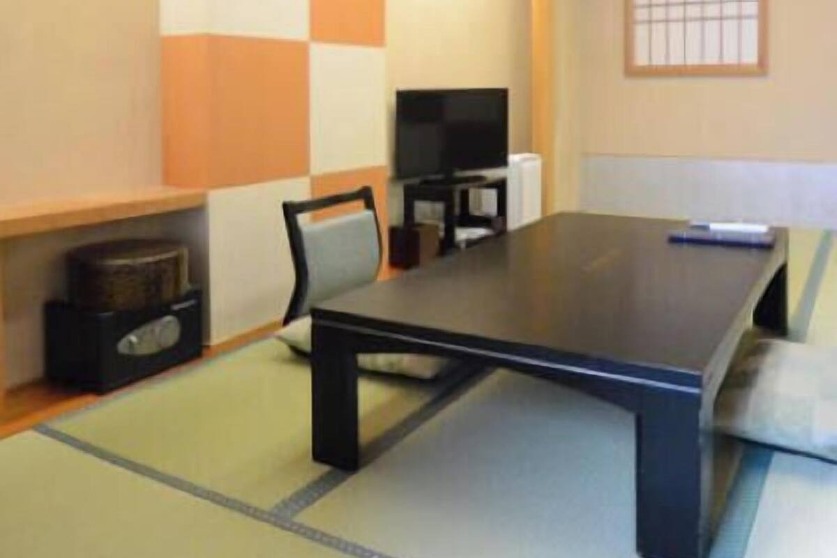 Une pièce avec un sol recouvert de tatamis, une table basse, une chaise, un téléviseur et une étagère sur laquelle se trouve un haut-parleur.