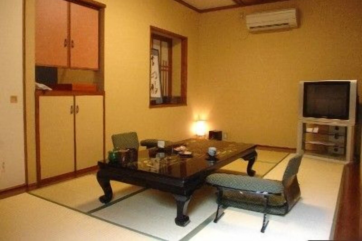 A traditional Japanese-style room with tatami flooring, a low table, chairs, a television, and a cabinet.