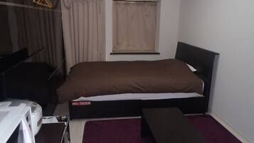 A compact room with a single bed, a small table, a microwave, and a window with curtains.