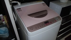 A front-loading washing machine with a control panel, a microwave above it, and a blue dish rack to the left.
