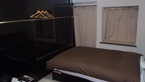 A bedroom with a bed, a TV, a desk with a computer, and a window with curtains.