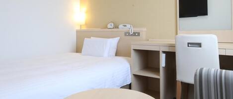 A hotel room with a bed, a desk, a chair, a round table, a wall-mounted TV, and a bedside lamp.
