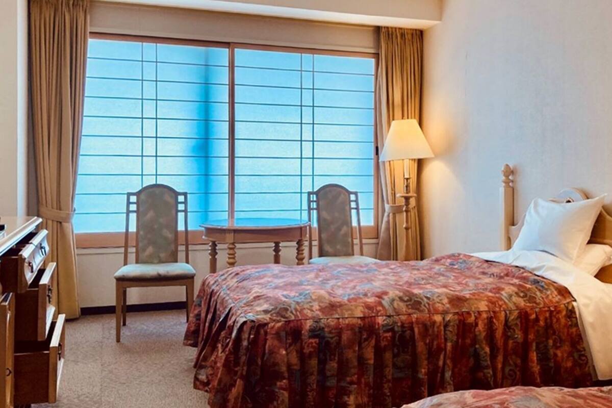 A hotel room with a bed, two chairs, a desk, a lamp, and a window with curtains.
