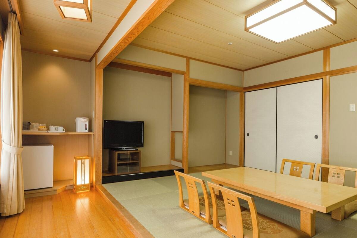 A traditional Japanese-style room with tatami flooring, a low table with chairs, a television, and sliding doors.