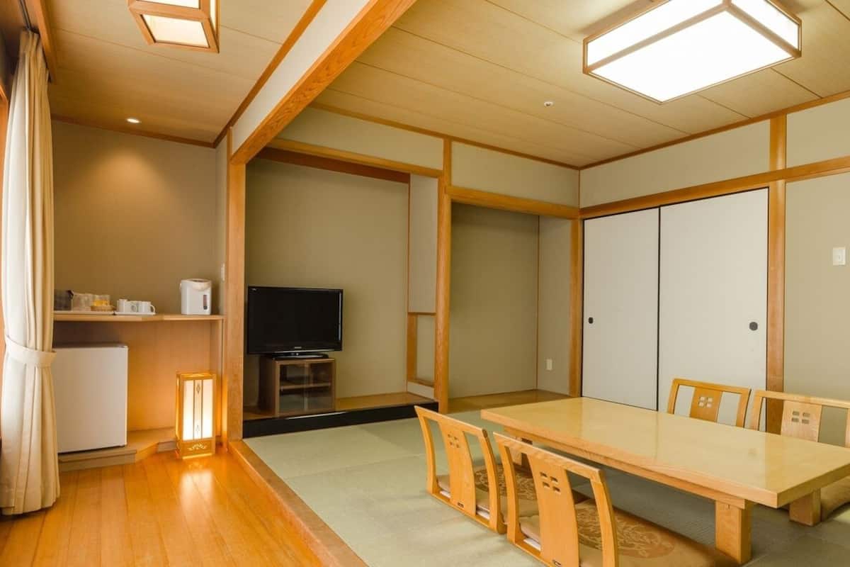 A traditional Japanese-style room with tatami flooring, a low table with chairs, a television, and sliding doors.