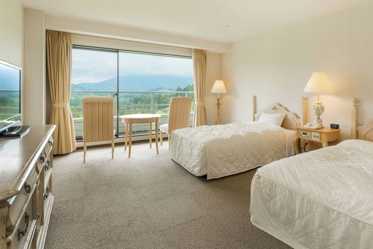 A hotel room with two beds, a desk, a chair, and a view of the mountains.